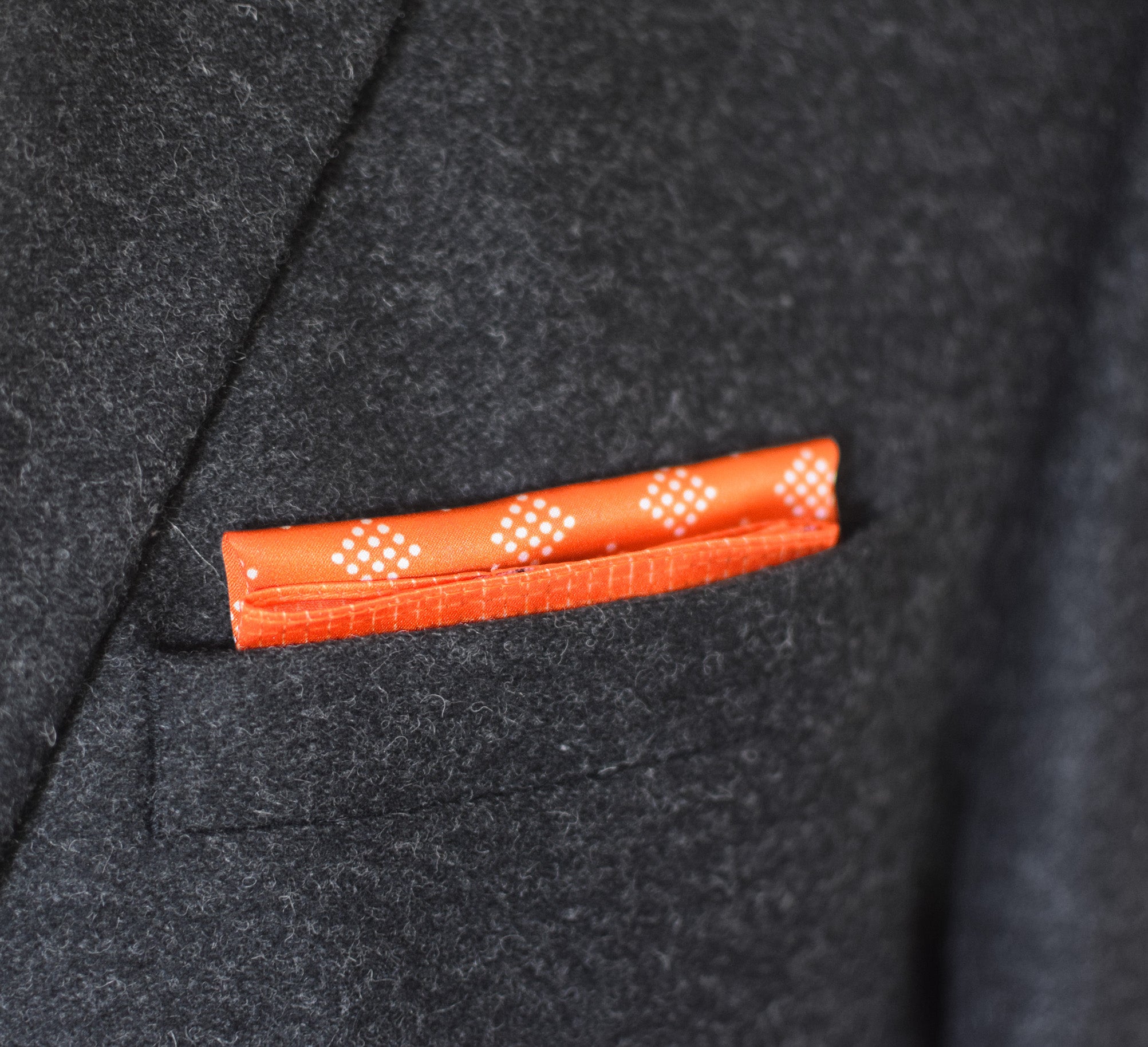 100% silk Batik Orange Pocket Square in orange by Laslett England shown folded into a flat square in a charcoal suit jacket pocket.