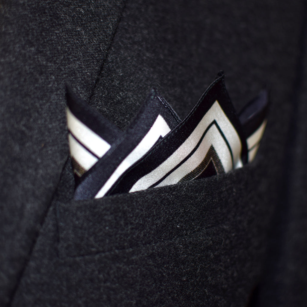 Laslett England Gambit Ivory pocket square in breast pocket of navy suit, black silk with white border and stripe detail.