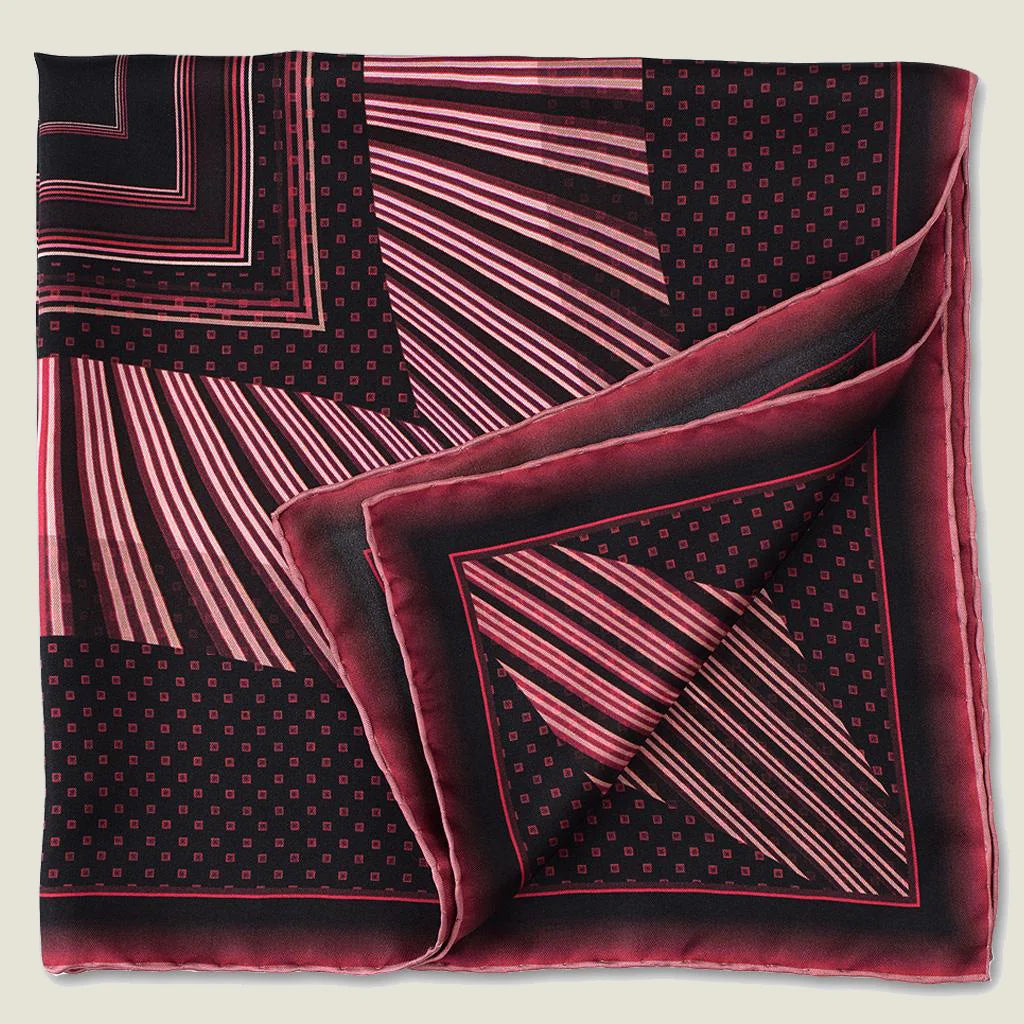 Houston Ruby Silk Bandana from Laslett England with a graphic radial stripe in ruby and rose pink pictured tied at the neck on a female model. Shown folded in four.