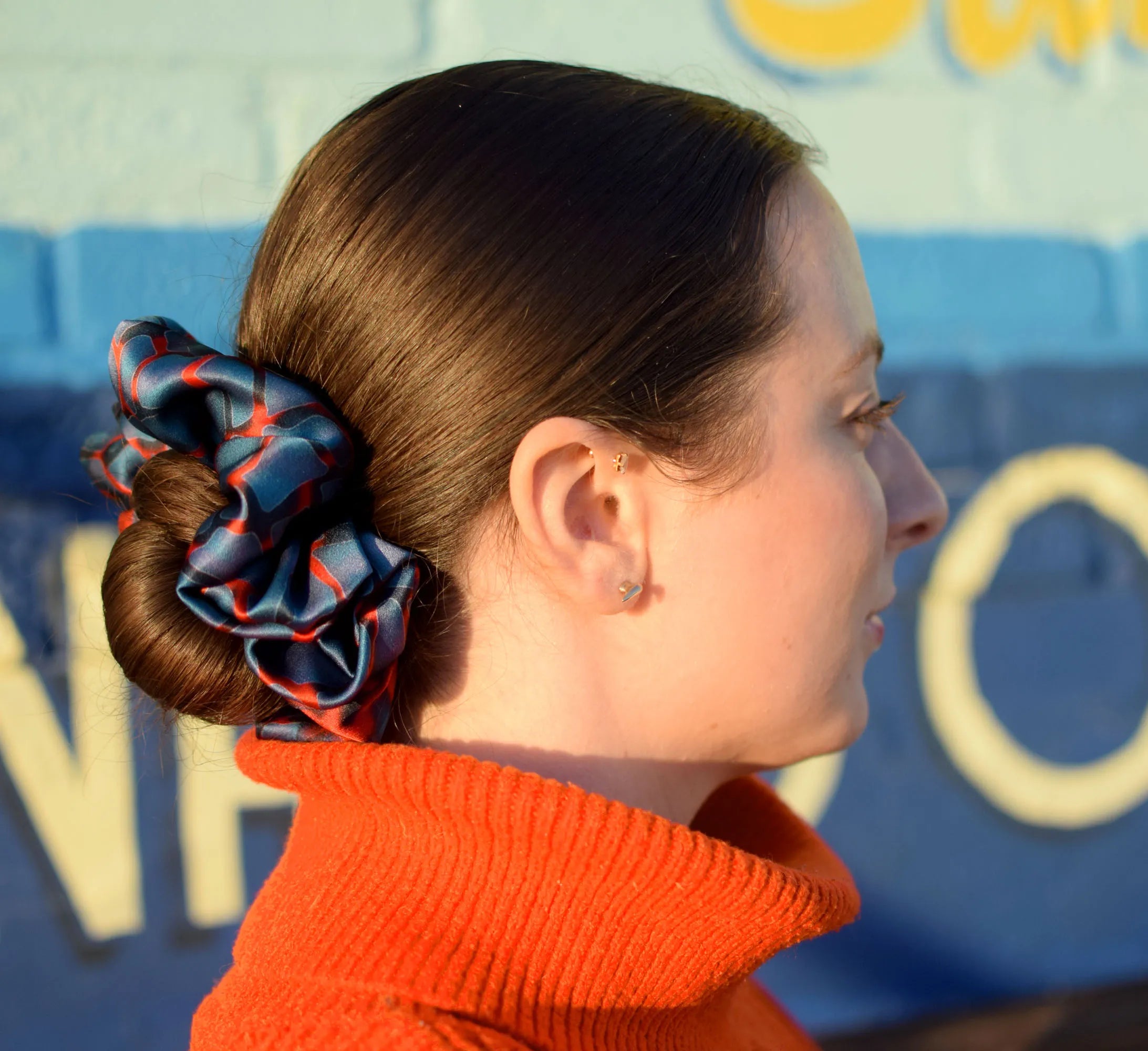 100% silk Chrome Blue Silk Scrunchie in blue by Laslett England photographed on a model in profile wearing a bun.