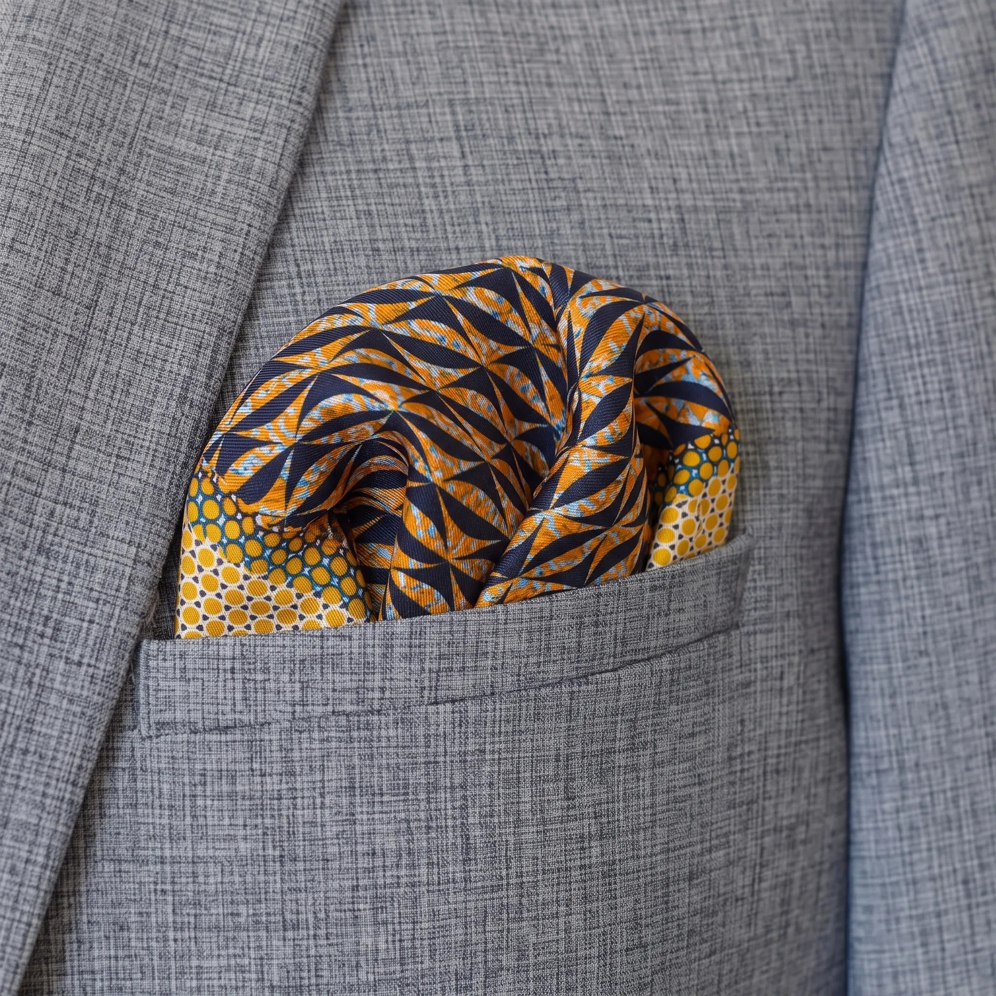 100% silk Havana Camel Pocket Square in gold and black with orange and green highlights by Laslett England. Scarf is shown in a puff in a grey suit pocket.
