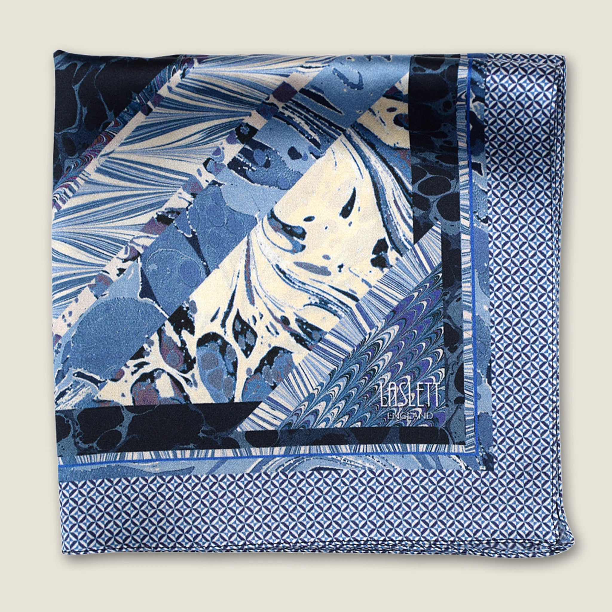 The Marble Blue pocket square print carries the flowing, layered quality of traditional hand-marbling in blue and cream tones with a geometric border. Photographed folded into four with the Laslett England logo on display.