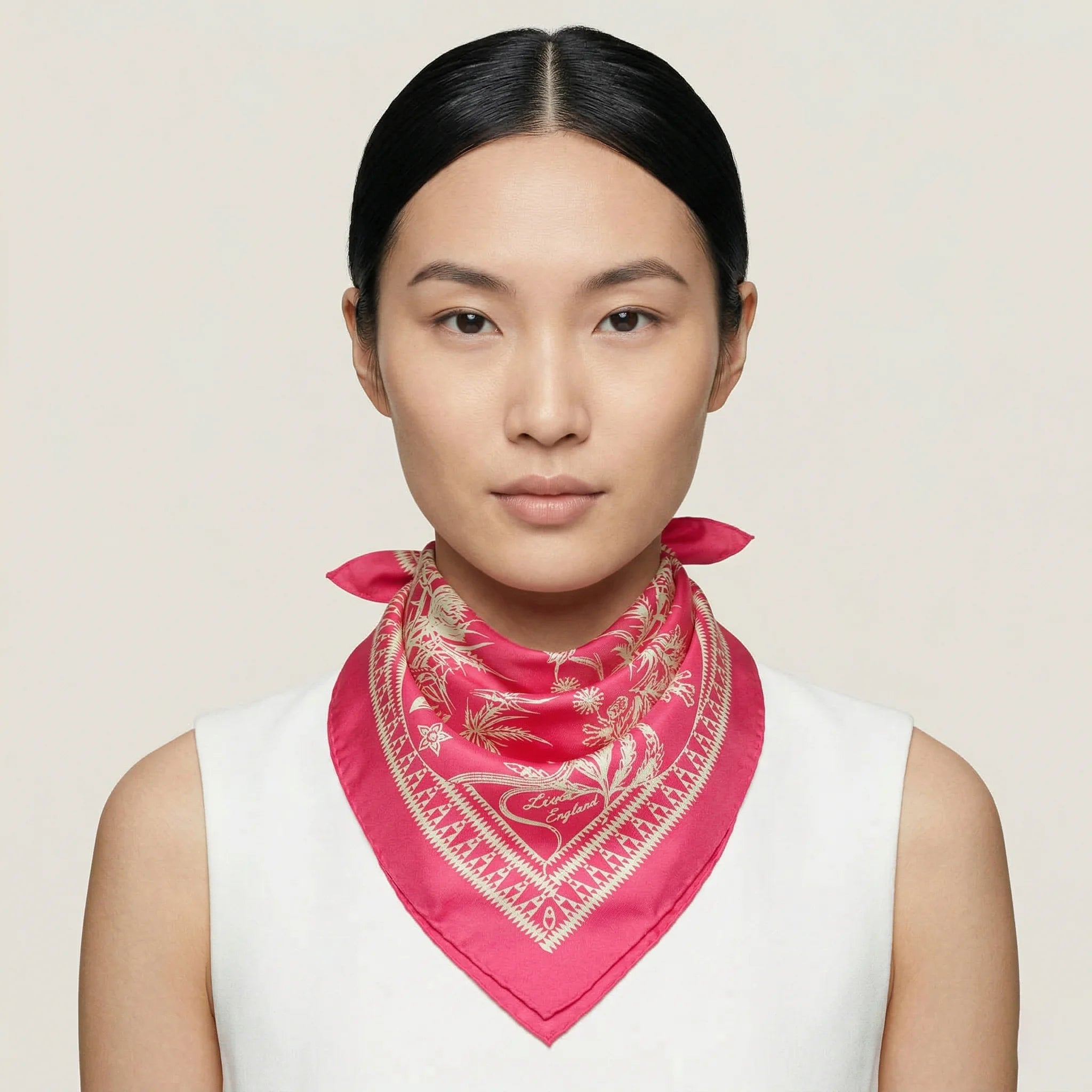 Laslett England Marettimo Cerise Silk Bandana worn knotted at neck by female model in white top, showing cerise pink with cream coastal print.