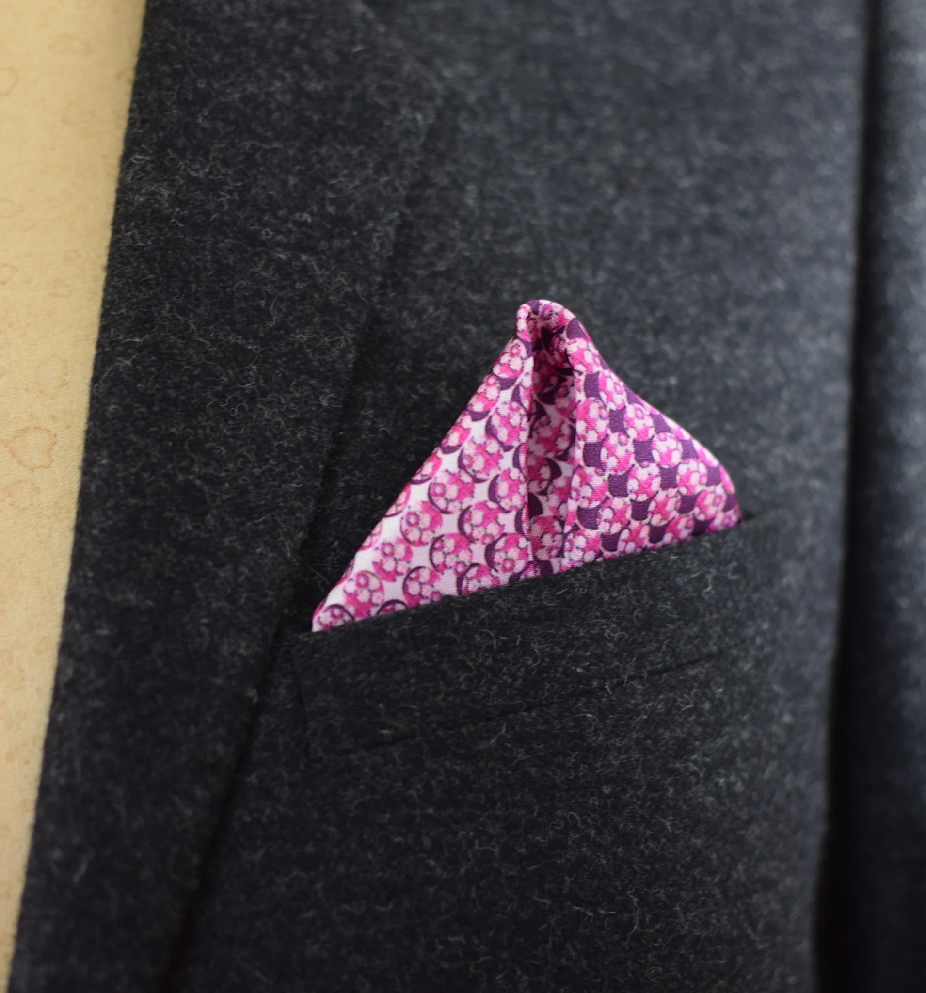 This Matrix Pink pocket square has a striking geometric design that reveals, on closer inspection, repeating graphic lines and patterns. In soft dusty pink with charcoal and white, square is shown folded into a neat triangle in a charcoal suit pocket.