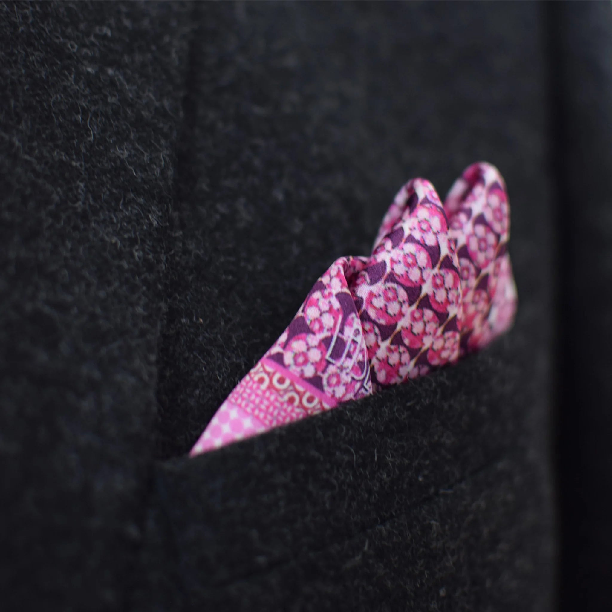 This Matrix Pink pocket square has a striking geometric design that reveals, on closer inspection, repeating graphic lines and patterns. In soft dusty pink with charcoal and white, square is shown tucked neatly into a charcoal suit pocket.