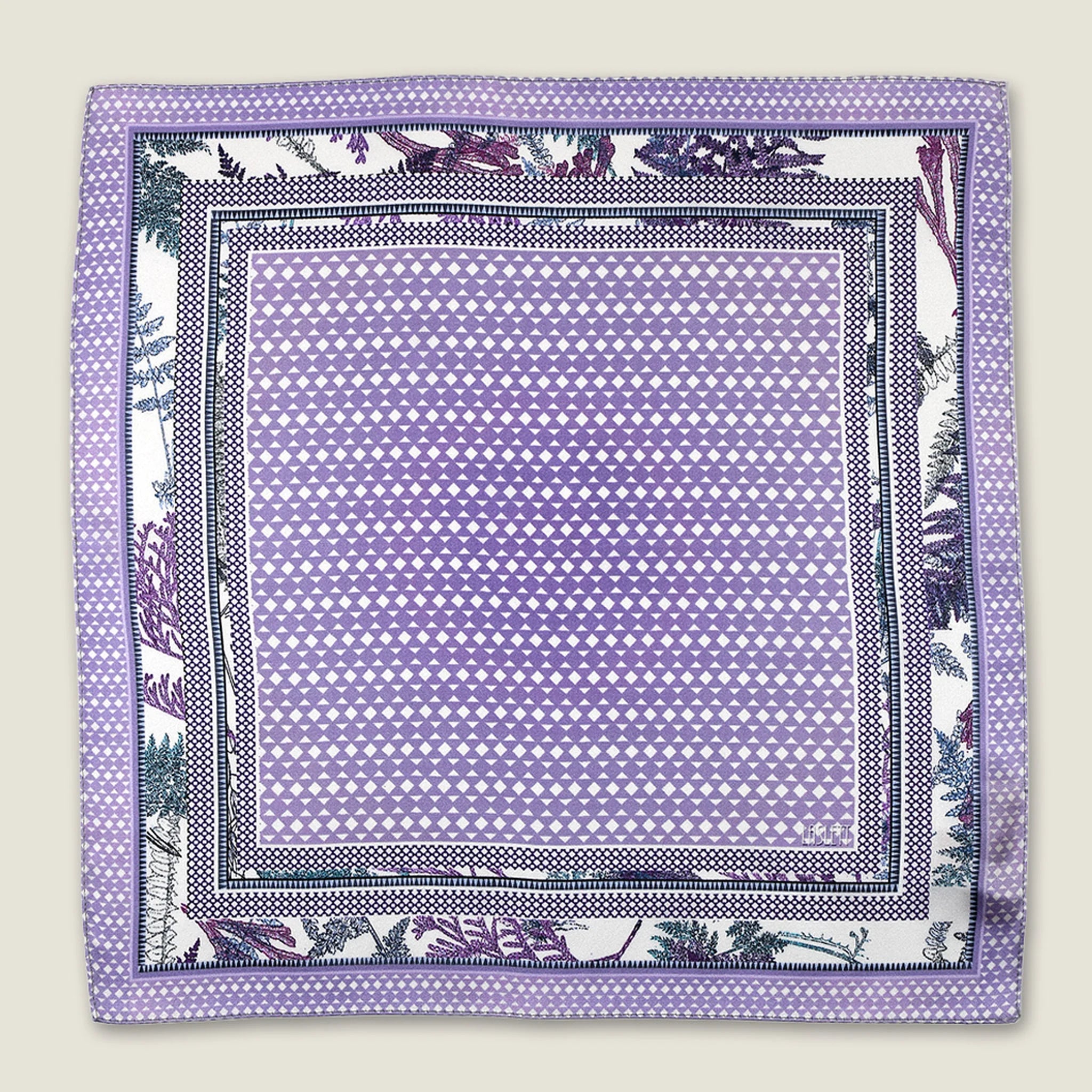 100% silk Panama Lilac pocket square takes its pattern from woven cane and straw, a geometric centre print in soft lilac and white with a botanical border of ferns in complementary tones. Photographed in flat lay.