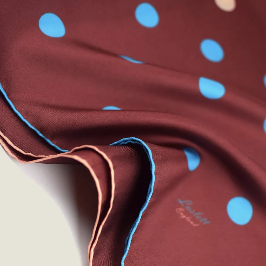 Laslett England Solitaire Chestnut Foulard shown in close up with the signature on display. Scarf is in chestnut silk satin with cornflower blue and cream polka dots.