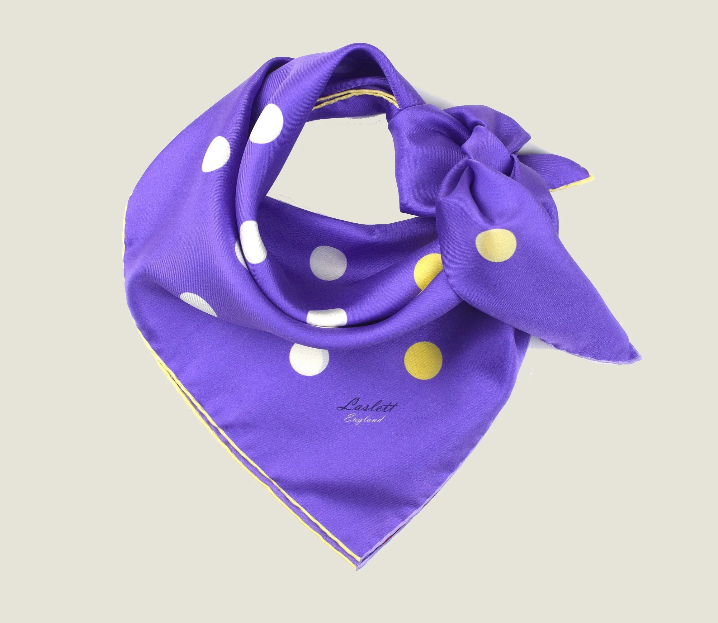 Laslett England Solitaire Violet Foulard folded into triangle, showing violet silk satin with lemon and cream polka dots and cream hand-rolled edge. Scarf is tied behind the neck.