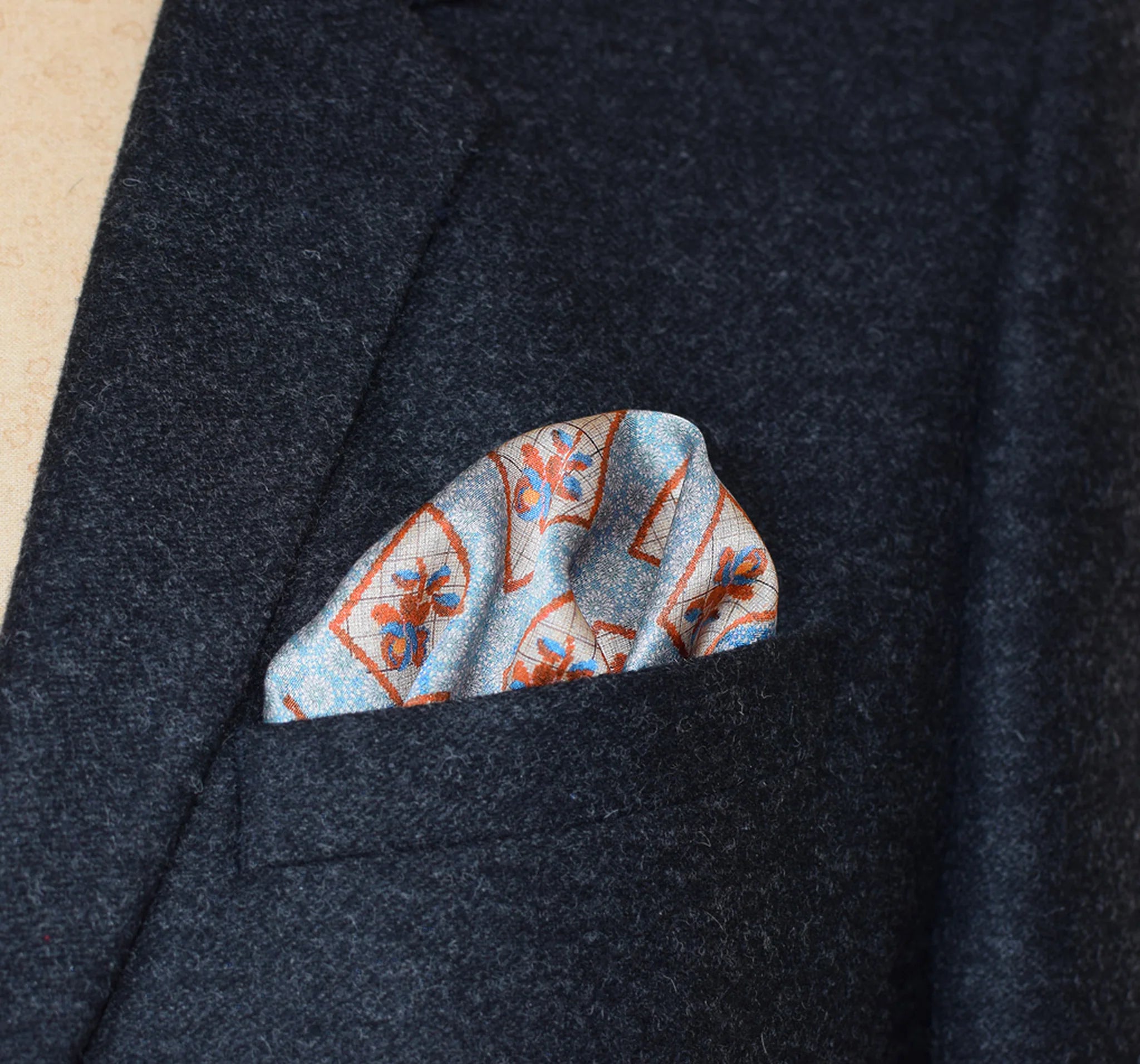 Laslett England Tapestry Rose silk pocket square in breast pocket of grey suit jacket, blue and terracotta print.