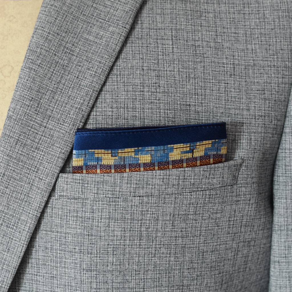 100% silk Aztec Blue Pocket Square in blue by Laslett England. Pocket square is shown neatly arranged in a grey suit jacket pocket. 