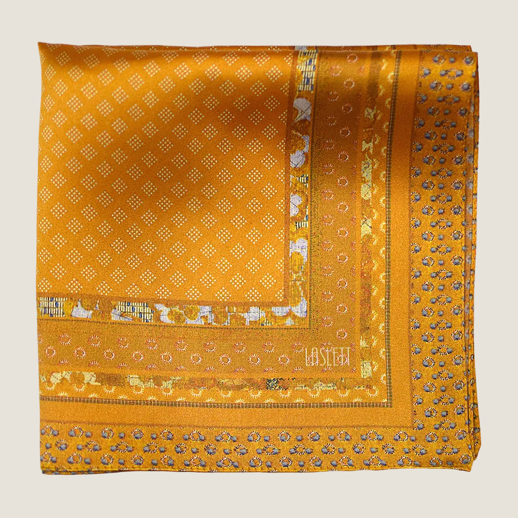 Batik Patchwork Gold pocket square in gold with an intricate patchwork of geometric patterns. Scarf is shown folded in four in flat lay. 