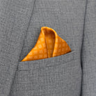 Batik Patchwork Gold pocket square in gold with an intricate patchwork of geometric patterns. Scarf is shown folded in the breast pocket of a grey suit. 