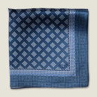 Batik Indigo pocket square has a deep ink blue ground with a geometric pattern in the batik tradition, finished with a gingham check border. Square is shown folded into four. 