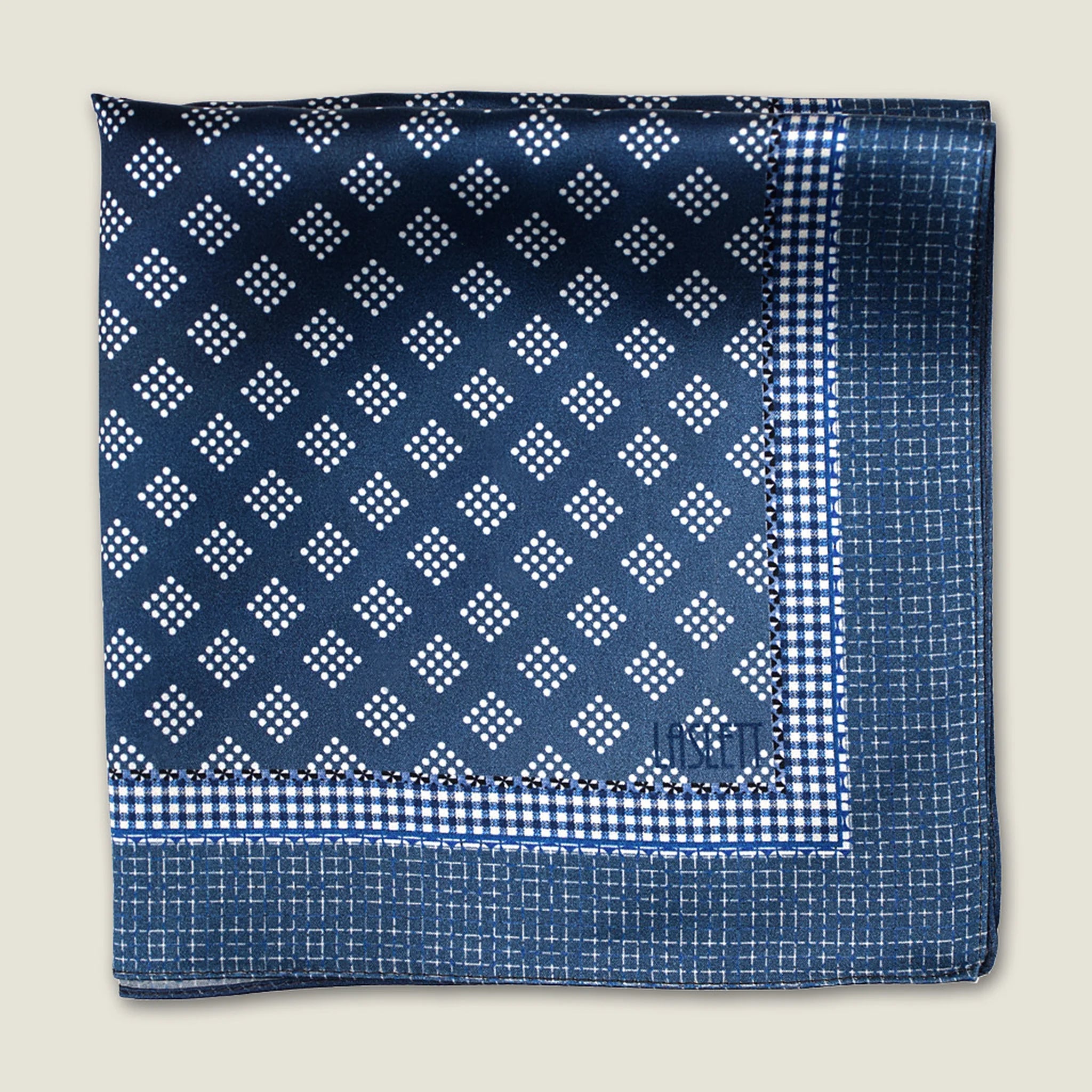 Batik Indigo pocket square has a deep ink blue ground with a geometric pattern in the batik tradition, finished with a gingham check border. Square is shown folded into four. 