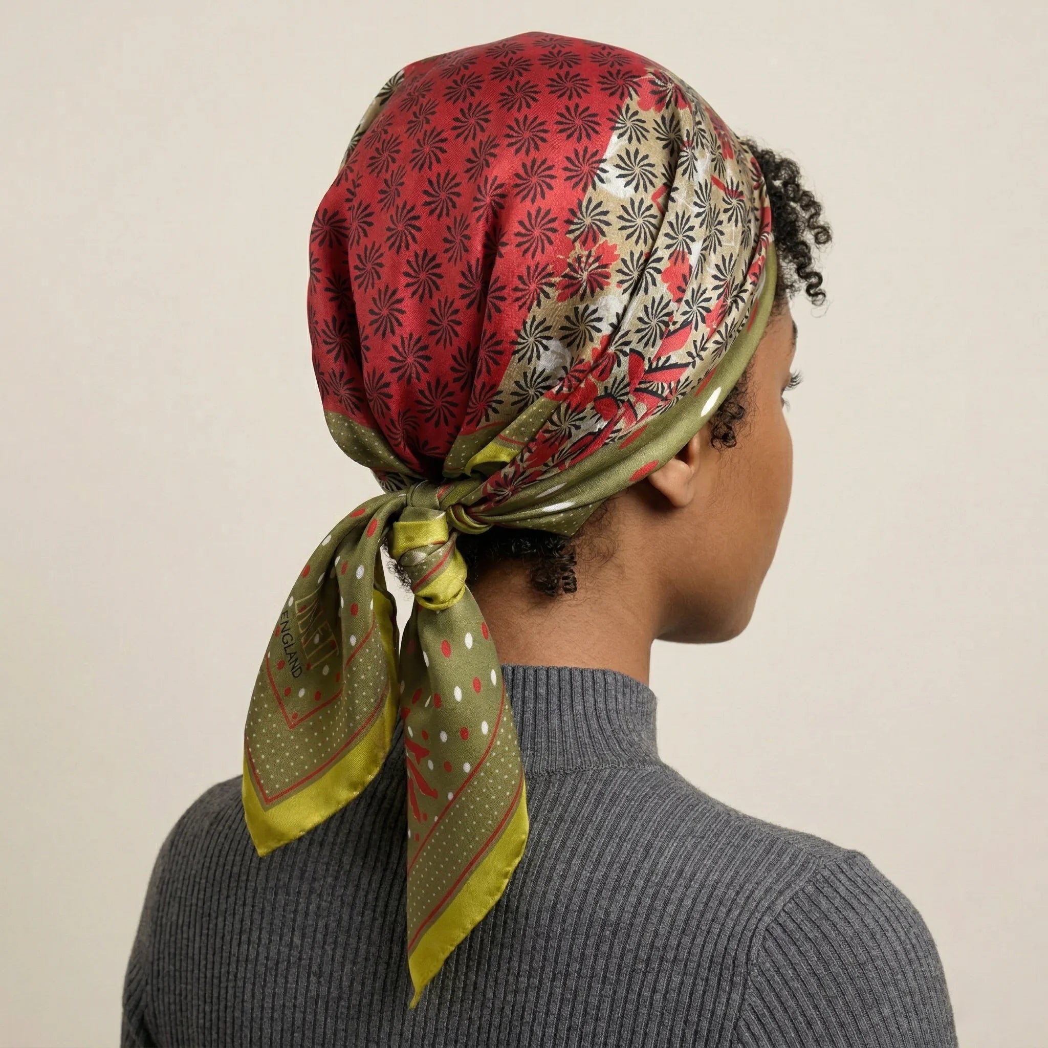 Laslett England Cadiz Silk Bandana worn as headscarf, rear view showing camel, olive, red and mustard gold radiating section print tied at nape.