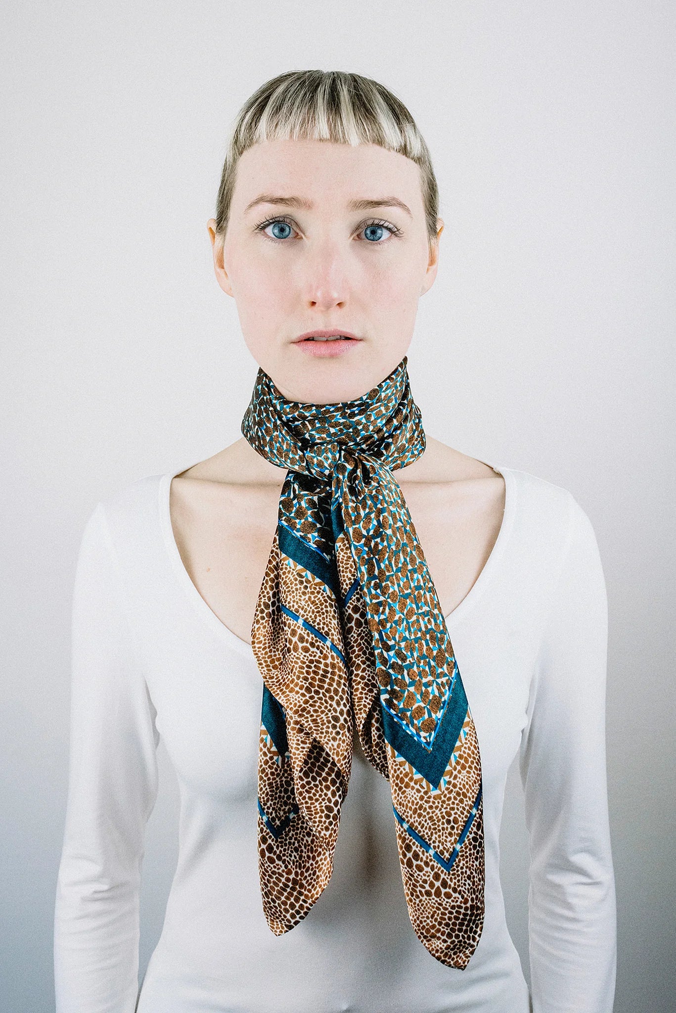 Laslett England classic square silk scarf tied at the neck, teal and bronze print worn with white shirt