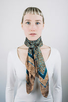 Laslett England classic square silk scarf tied at the neck, teal and bronze print worn with white shirt