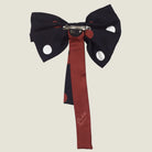 100% silk Coco Silk Bow in black and red by Laslett England. Photographed in reverse showing a badge fastening and barette with a red ribbon and 'Laslett England' logo. 