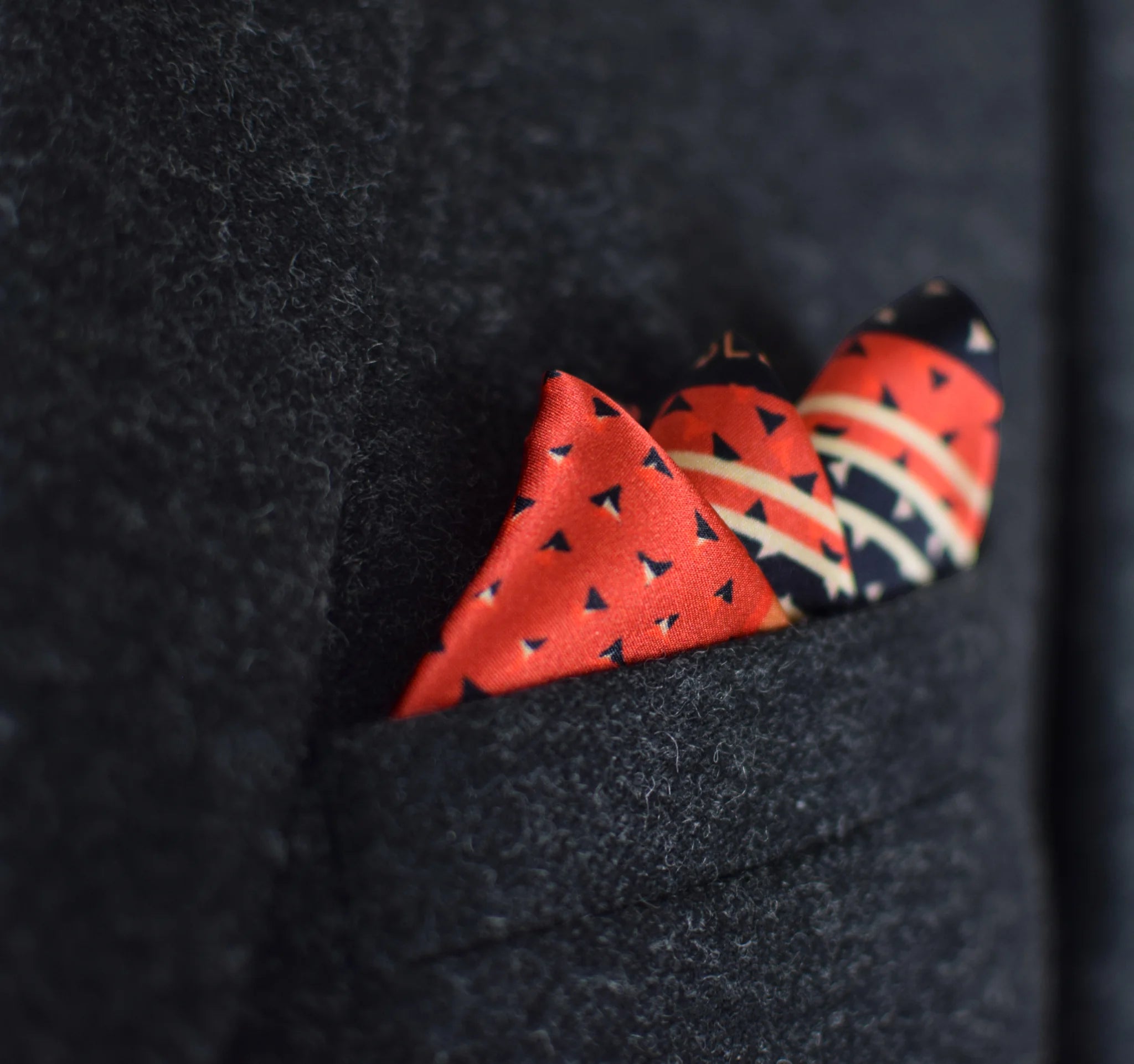 Laslett England Deco Noir silk pocket square in breast pocket, black and red geometric print with pocket point showing.