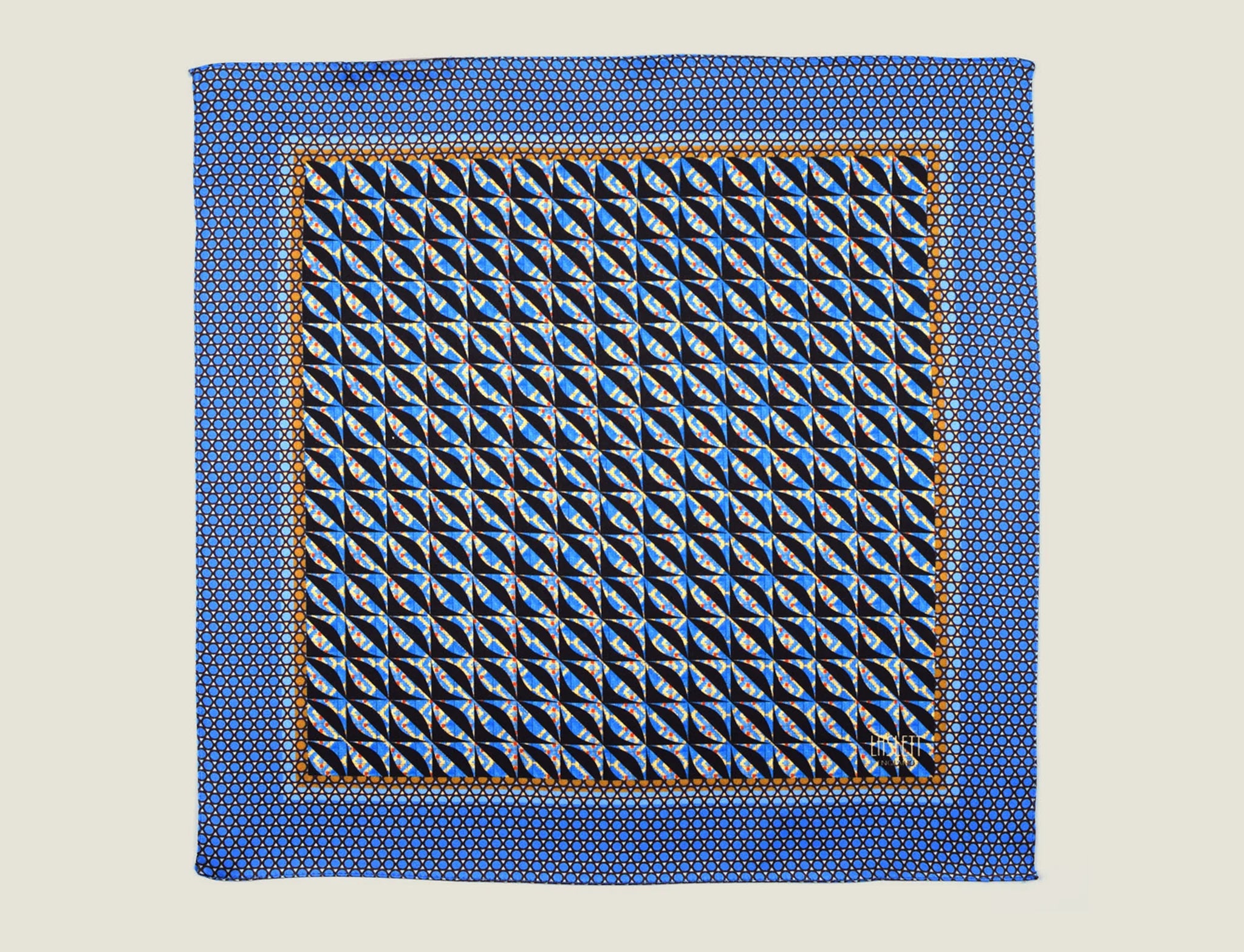 The 100% silk Havana Blue pocket square has a pale blue ground with a diamond repeat carrying small floral motifs in orange, red and cream, finished with a fine geometric border. Square is shown in flat lay on a neutral border. 