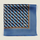The 100% silk Havana Blue pocket square has a pale blue ground with a diamond repeat carrying small floral motifs in orange, red and cream, finished with a fine geometric border. Square is shown folded into four in flat lay on a neutral background. 