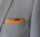 100% silk Marble Amber pocket square is inspired by the decorative marbled papers found inside antique and fine books. Shown folded into a neat square in a grey suit jacket that shows both the border and the central section. 