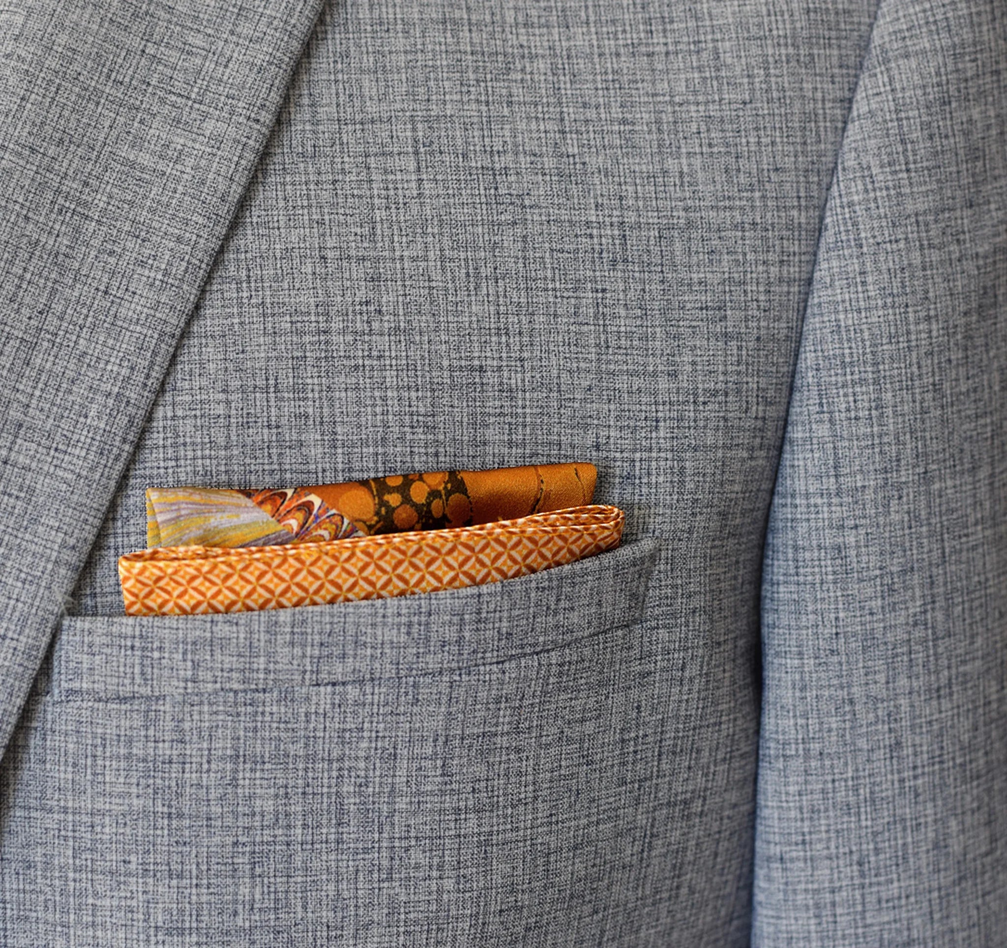 100% silk Marble Amber pocket square is inspired by the decorative marbled papers found inside antique and fine books. Shown folded into a neat square in a grey suit jacket that shows both the border and the central section. 