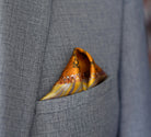 100% silk Marble Amber pocket square is inspired by the decorative marbled papers found inside antique and fine books. Shown tucked neatly in a triangle inside a grey suit jacket. 