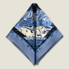 The Marble Blue pocket square print carries the flowing, layered quality of traditional hand-marbling in blue and cream tones with a geometric border. Photographed folded into two triangles on a neutral background. 