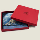 The Marble Blue pocket square print carries the flowing, layered quality of traditional hand-marbling in blue and cream tones with a geometric border. Photographed folded in the red signature box. 