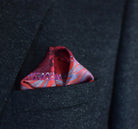 100% silk Marble Red pocket square print carries the flowing, layered quality of traditional hand-marbling in deep red and cream tones with a geometric border. Photographed folded into a triangle in a dark suit pocket. 