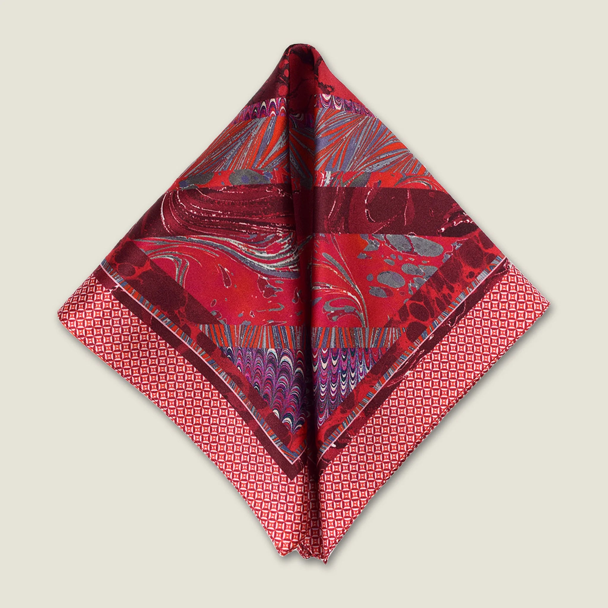 100% silk Marble Red pocket square print carries the flowing, layered quality of traditional hand-marbling in deep red and cream tones with a geometric border. Photographed folded into a triangle on a neutral background. 