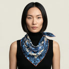 100% silk triangle Marble Rose Triangle Scarf in blue by Laslett England. Shown tied at the neck and worn by a model pictured against a neutral background. 
