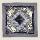 The 100% silk Marble Slate Pocket Square centre field carries multiple marble techniques including feathered combing, stone drop patterns and swirled forms in slate grey, charcoal and dusted lilac, with a geometric tiled border. Photographed in flat lay. 