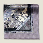 The 100% silk Marble Slate Pocket Square centre field carries multiple marble techniques including feathered combing, stone drop patterns and swirled forms in slate grey, charcoal and dusted lilac, with a geometric tiled border. Photographed folded into four with the Laslett England logo on display. 