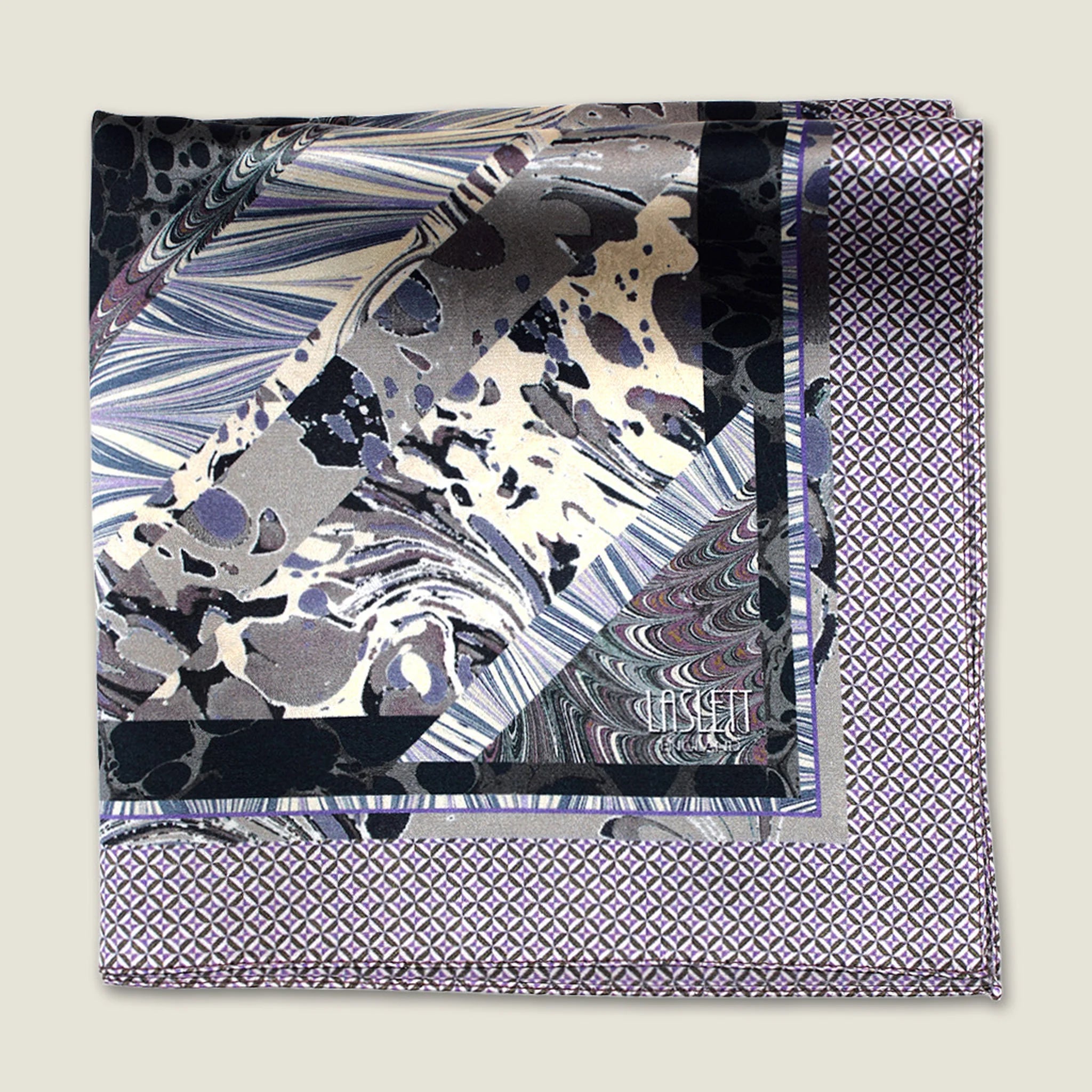 The 100% silk Marble Slate Pocket Square centre field carries multiple marble techniques including feathered combing, stone drop patterns and swirled forms in slate grey, charcoal and dusted lilac, with a geometric tiled border. Photographed folded into four with the Laslett England logo on display. 