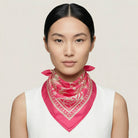 Laslett England Marettimo Cerise Silk Bandana worn knotted at neck by female model in white top, showing cerise pink with cream coastal print.