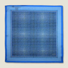 100% silk Matrix Blue pocket square has a distinctive geometric and repeating floral print in blue tones. Shown displayed in flat lay on a neutral background. 