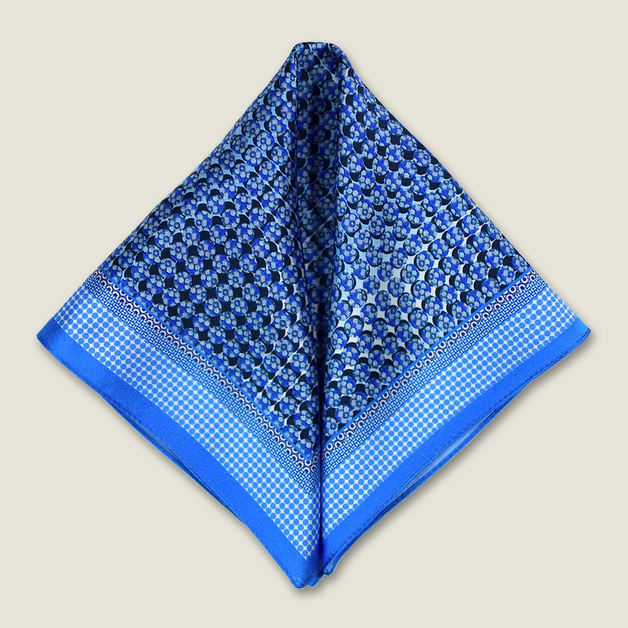 100% silk Matrix Blue pocket square has a distinctive geometric and repeating floral print in blue tones. Shown folded into two triangles against a neutral background. 