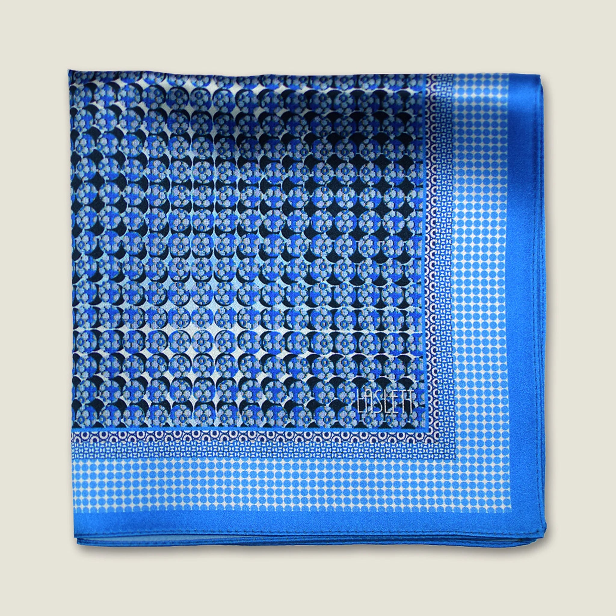 100% silk Matrix Blue pocket square has a distinctive geometric and repeating floral print in blue tones. Shown folded in four against a neutral background. 