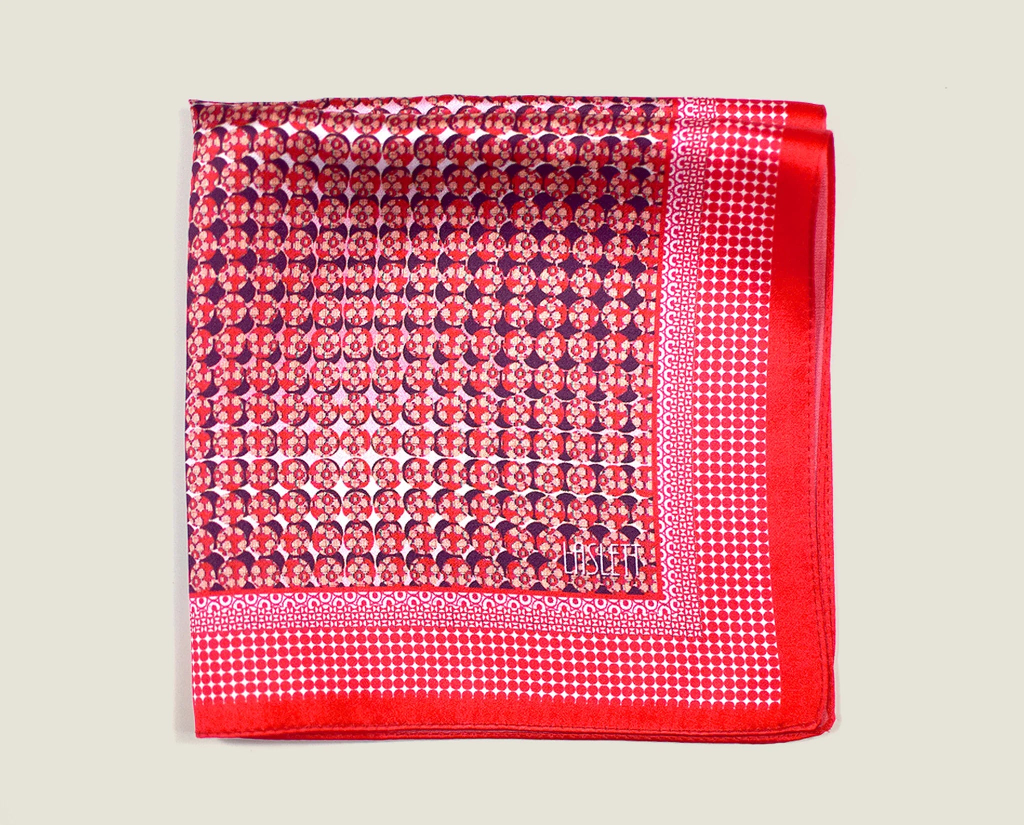 100% Matrix Red pocket square has a geometric design with a floral repeat that reveals itself on closer inspection. Square is shown folded into four on a neutral background. 