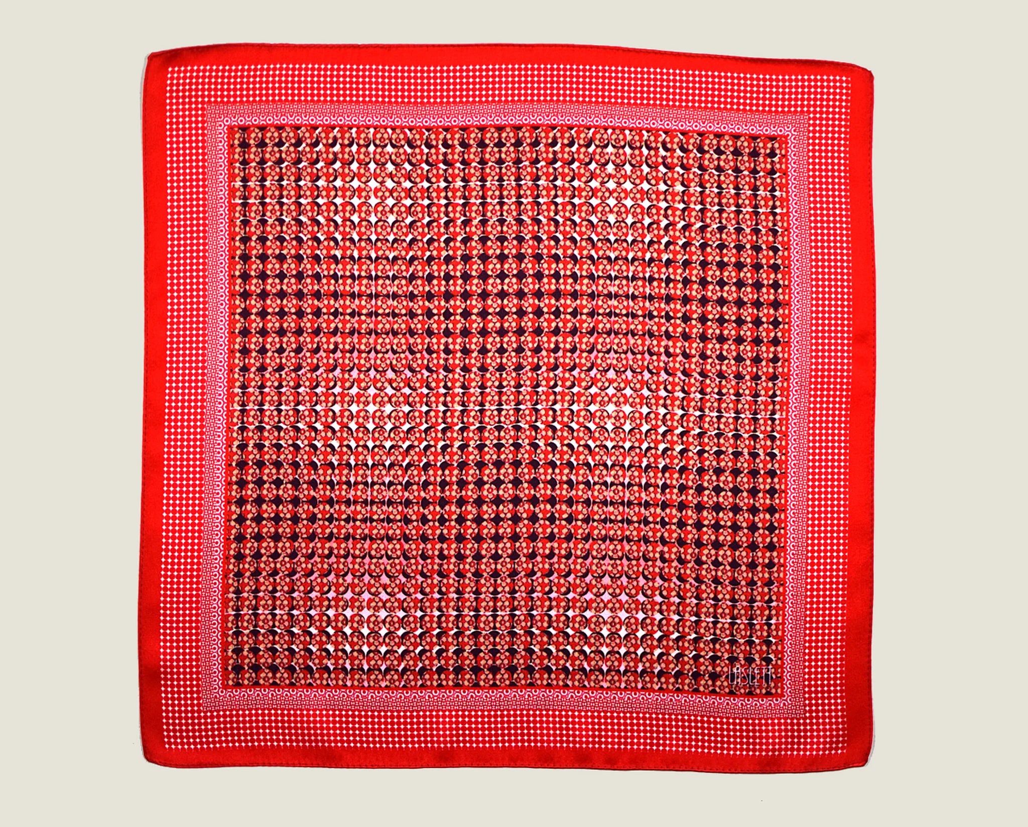 100% Matrix Red pocket square has a geometric design with a floral repeat that reveals itself on closer inspection. Square is shown in flat lay against a neutral background. 