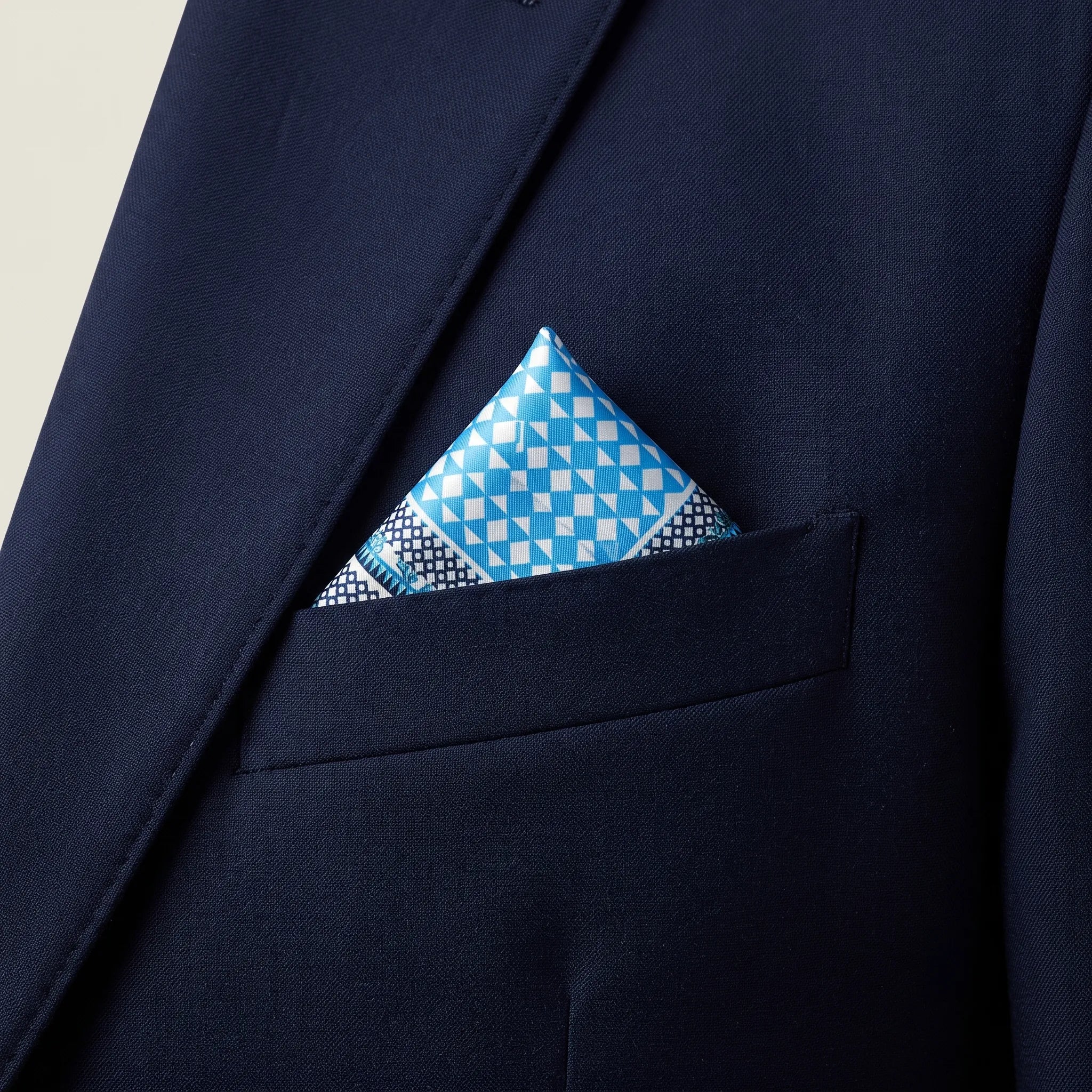 Laslett England Panama Blue silk pocket square in breast pocket of navy suit, turquoise diamond pattern with white folded edge showing
