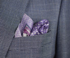 100% silk Panama Lilac pocket square takes its pattern from woven cane and straw, a geometric centre print in soft lilac and white with a botanical border of ferns in complementary tones. Photographed loosely arranged into a suit jacket. 