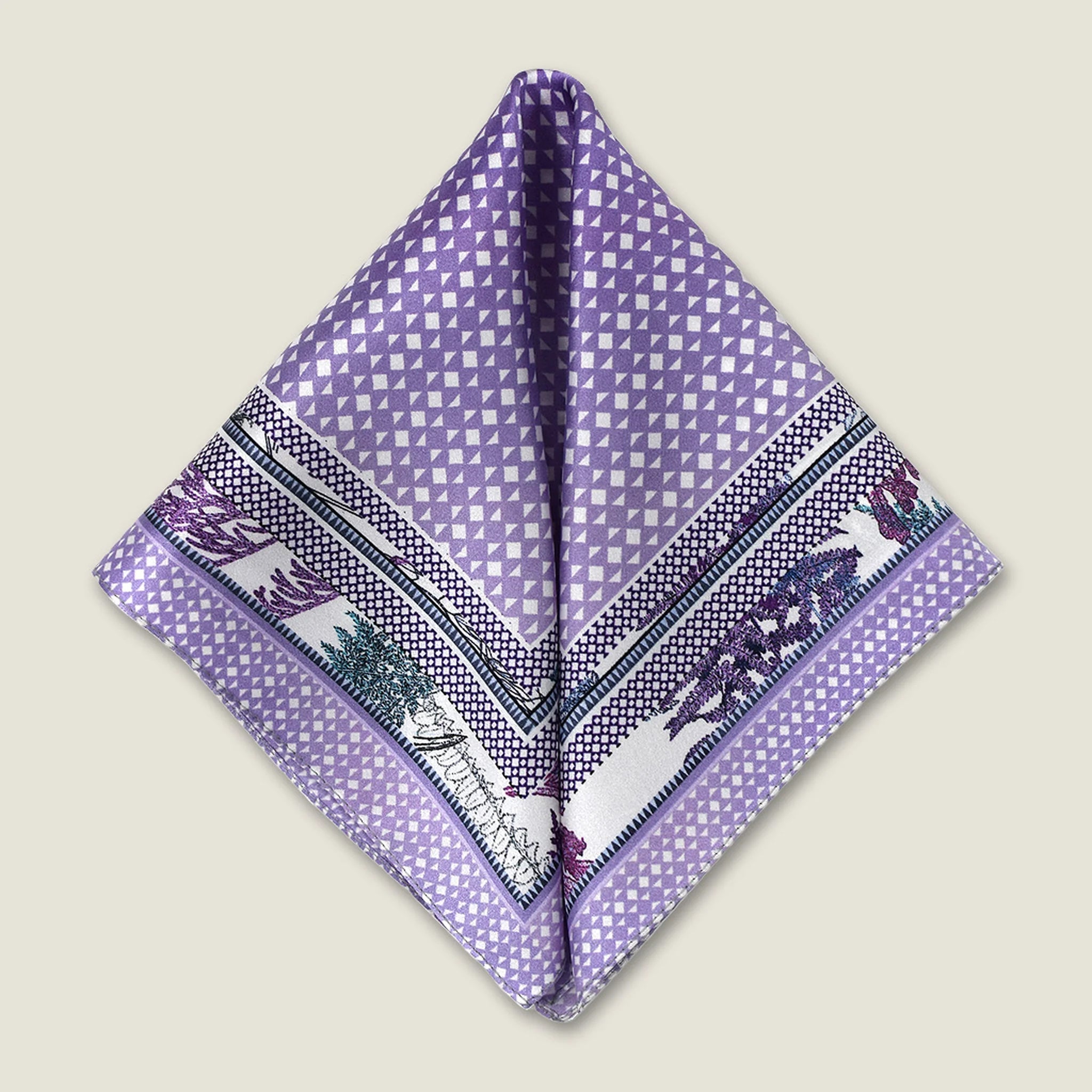 100% silk Panama Lilac pocket square takes its pattern from woven cane and straw, a geometric centre print in soft lilac and white with a botanical border of ferns in complementary tones. Photographed folded into two triangles in flat lay. 