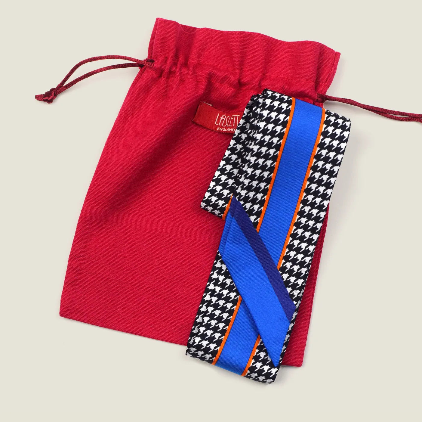 100% silk Dogtooth Blue Laslett Ribbon in black and blue by Laslett England. Ribbon is pictured on top of the red Laslett England presentation pouch. 