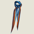 100% silk Sunset Orange Laslett Diamond in orange and blue by Laslett England. Scarf is shown tied around the neck against a neutral background. 
