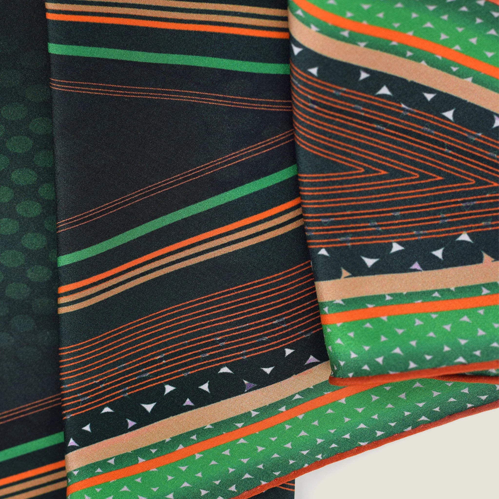 100% silk Riviera Emerald Laslett Diamond in orange; green; geometric by Laslett England. Scarf is pictured in close-up folded three times to show the orange detail and triangle pattern. 