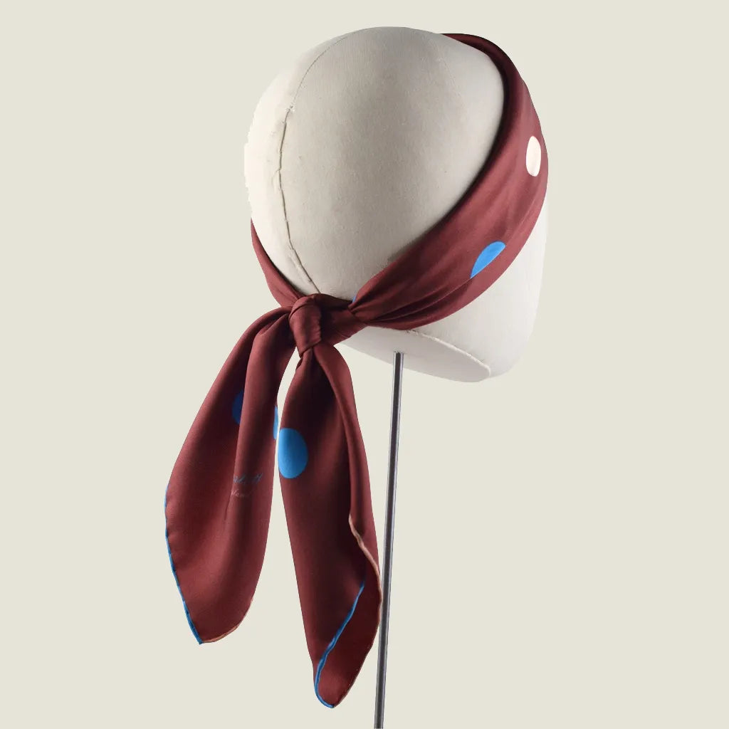 Laslett England Solitaire Chestnut Foulard worn as folded bandana on mannequin Scarg is in chestnut silk satin with cornflower blue and cream polka dots, knotted at nape.