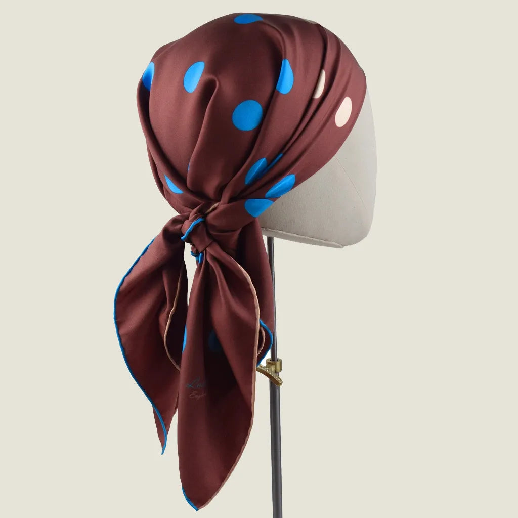 Laslett England Solitaire Chestnut Foulard worn as headscarf on mannequin, chestnut silk satin with cornflower blue and cream polka dots, knotted at nape.